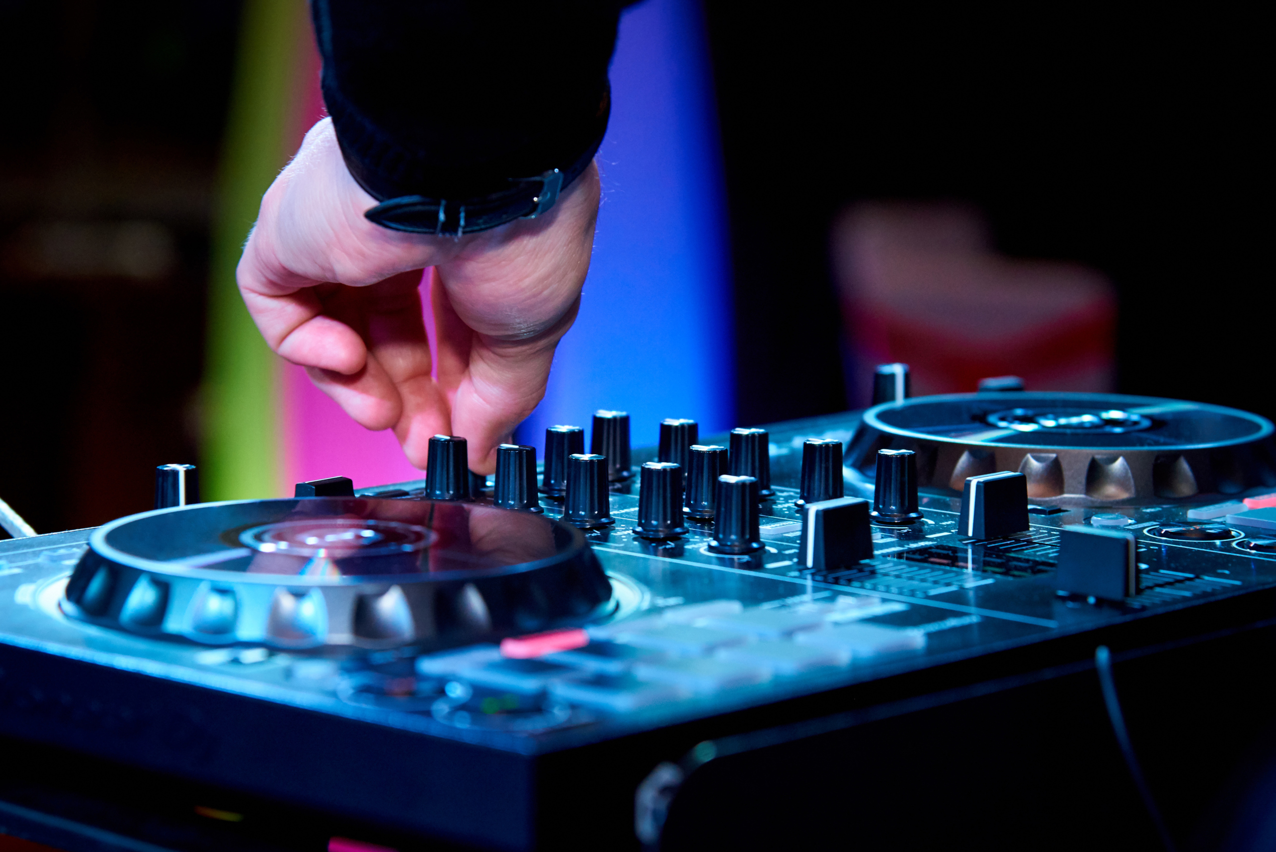 Close-up of male dj hands on a control panel under spotlights.